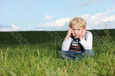 Glum little boy sitting in grass