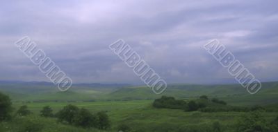 Stormy sky over green field and mountains