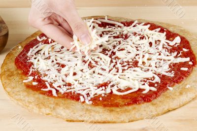 hand spreading cheese on a pizza dough 