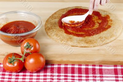 spreading tomato sauce on a pizza dough 
