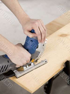 hand using electric jigsaw to cut wooden sheet