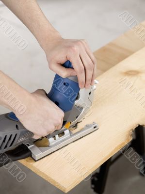 human hand holding jigsaw and cutting a piece of wood