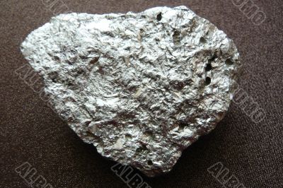 Silvery shiny stone on a dark brown background.