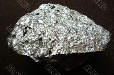 Silvery shiny stone on a dark brown background.