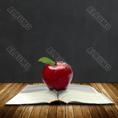 apple on a book with black board at the back