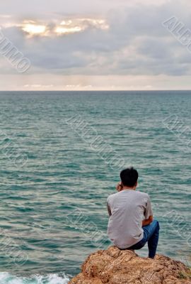 A man looks into the sea while sitting on a rock 