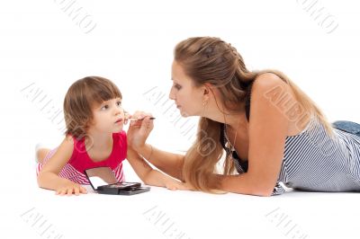 Young mother paints lipstick little daughter in the studio