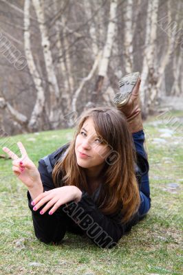 Young beautiful girl lying on the grass and shows a sign of peac