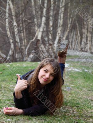 Young beautiful girl lying on the grass and shows OK hand sign