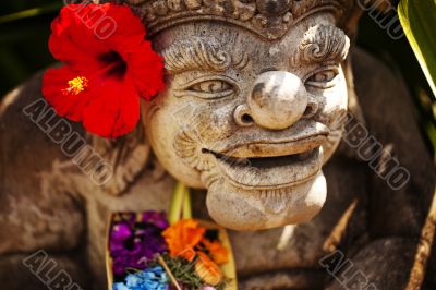 Face of statue with red flower.