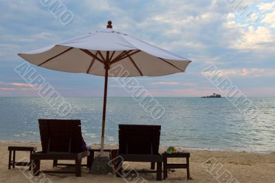 Two beds and an umbrella on the beach at sunset