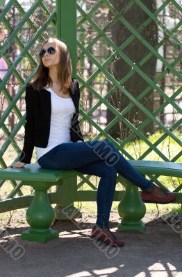 portrait of the beautiful girl sits on a bench in green park
