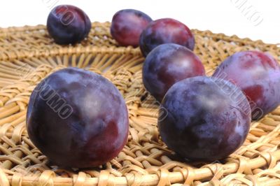 Ripe plums wicker dish on a white background.