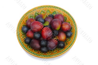 Ripe plums and prunes on ceramic dish on a white background.