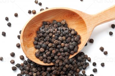 Black Peppercorn is strewed from a wooden spoon.