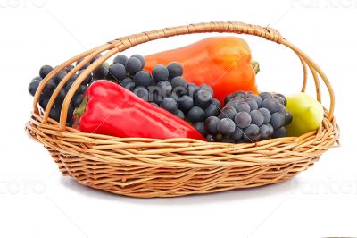Red, yellow pepper and grapes in a wicker basket on a white back