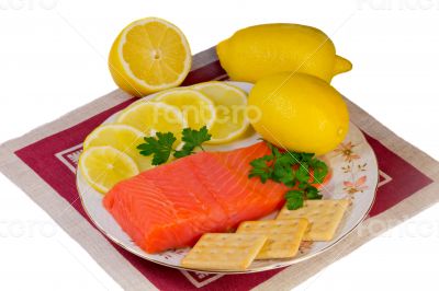 Salmon fillet and lemons on a platter on a white background.