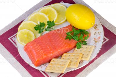 Salmon fillet and lemons on a platter on a white background.