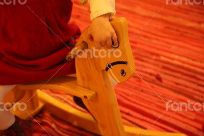 A small girl is riding wooden horse-rocking chair.