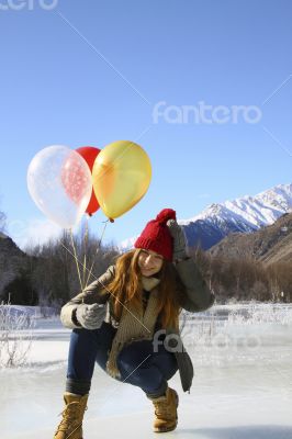 Happy girl with balloons on the ice against the background of sn