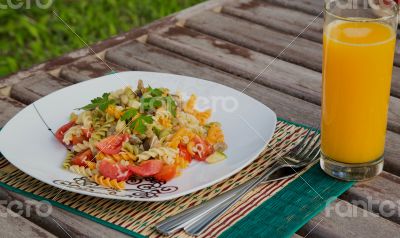 Pasta with vegetables and a glass of fresh orange juice