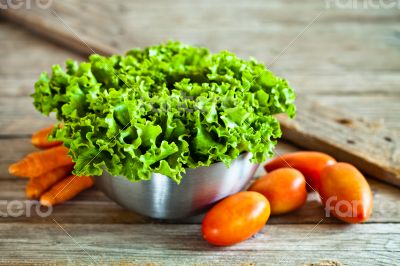 lettuce salad in metal bowl, tomatoes and carrots 