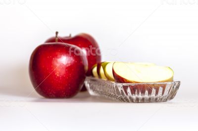 Two ripe red apples and segments of apple on a plate
