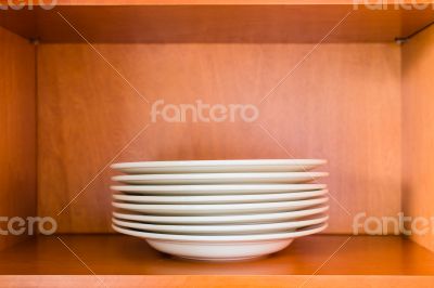 Organized minimalistic kitchen cabinet with a stack of white por