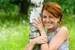 Smiling girl embrace a birch tree