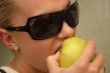 Girl in sun glasses eats green apple