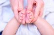 Mother hold baby leg in hand like rose flower