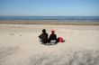 Woman and Man Sitting on Sand Watching Sea in Spring