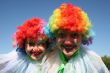 Two bizzare clowns in colored wigs upon blue sky