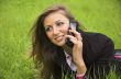 The girl speaks by phone laying on a green grass