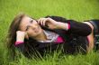 The girl speaks by phone laying on a green grass