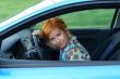 Young red-haired woman is siting in a car. Woman is happy
