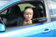 young blond woman in a blue car. She is smiling happy