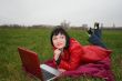 black head woman is laying on a plaid in park grass with notebook