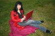 black head woman is sitting on a plaid in park grass with notebook