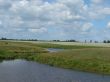 wide summer field with river uder cloudy blue sky