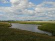 wide summer field with river uder cloudy blue sky