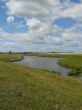 wide field with river uder cloudy deep blue sky