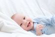Little joyful baby resting on white bed