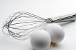 High contrast tilted view of a whisk and 2 eggs