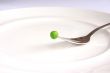 Single fresh green pea above white plate on fork.