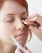 beautician is doing make-up to red-haired woman