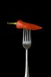 Red pepper on a silver for against a black background