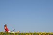 Girl relaxing with laptop in flowering field