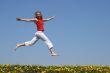 Girl flying in a jump over dandelion field
