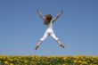 Girl flying in a funny jump over dandelion field